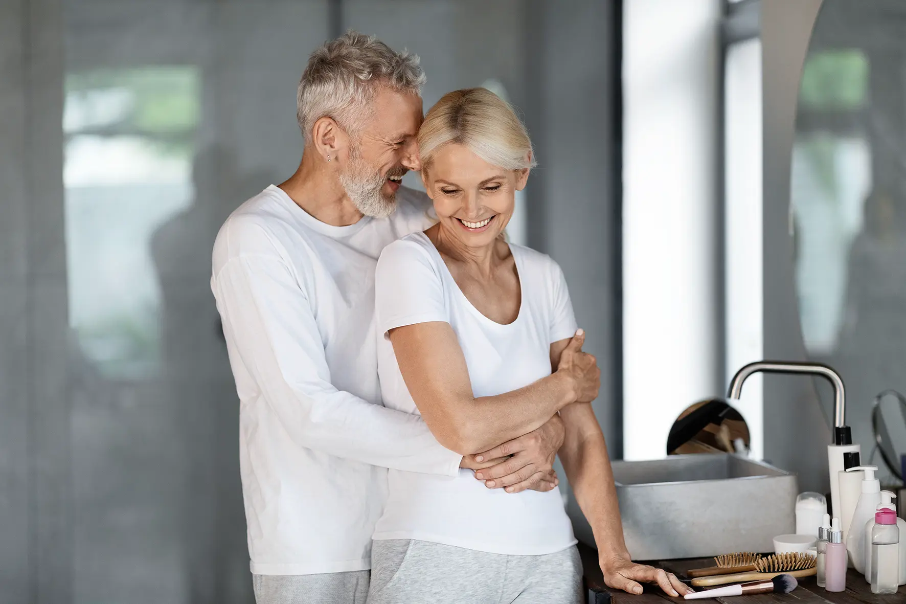 Glückliches älteres Ehepaar, das sich nach erfolgreicher All-on-4 Zahnersatzbehandlung umarmt und Lebensfreude zeigt.